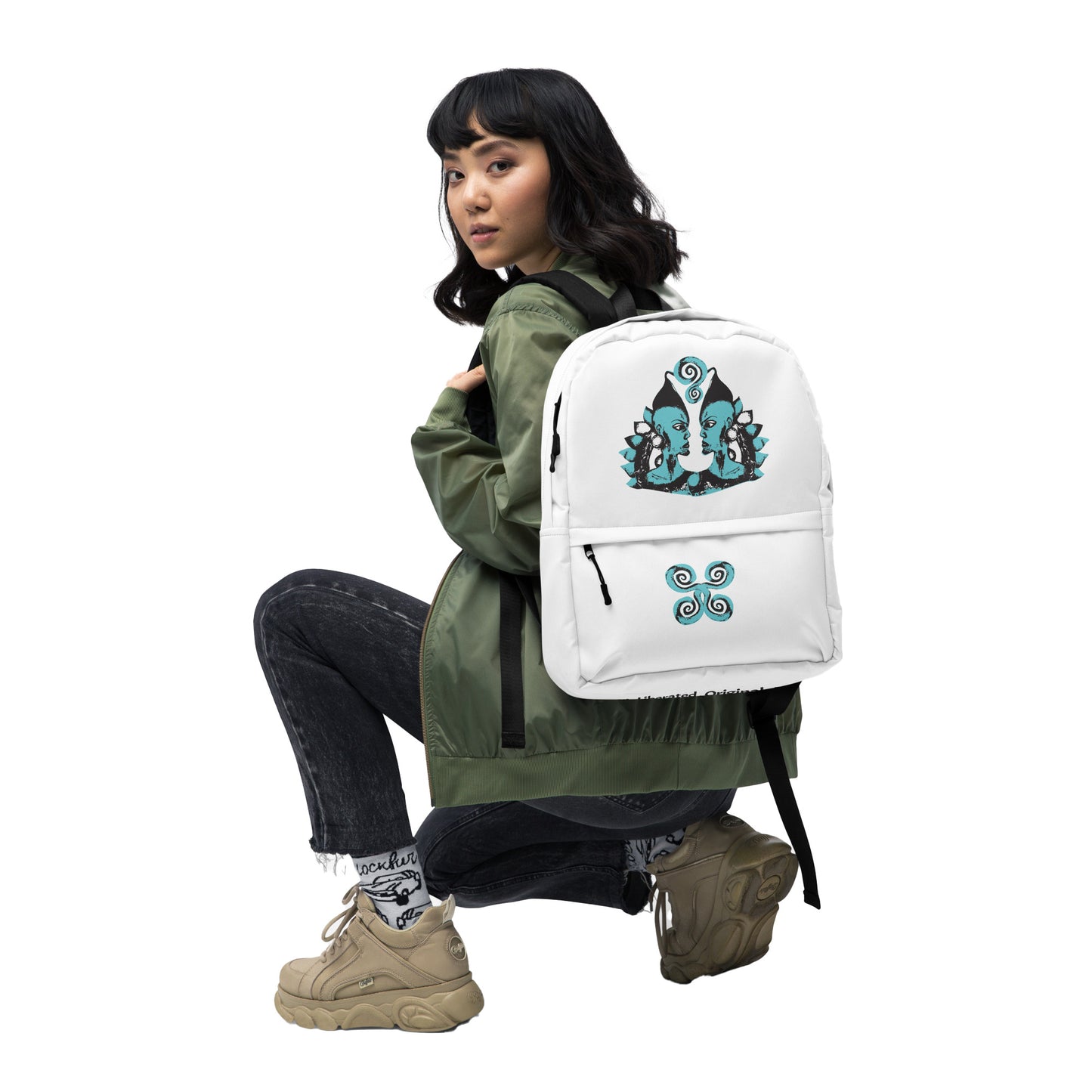 The model wearing a white backpack, featuring a hand-drawn, culturally inspired design of two mirrored faces in bold black and teal on the main panel, and an intricate teal spiral motif on the pocket, celebrating self-expression and individuality in modern bohemian style fashion by K.L.O.E.