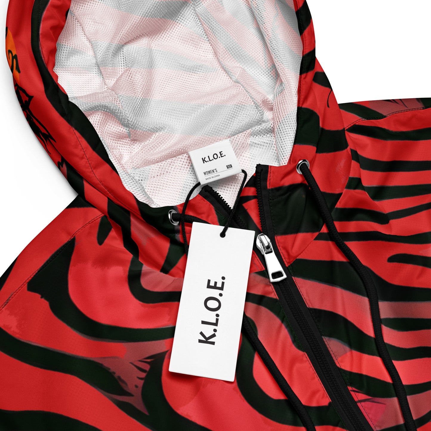 The detailed view of red and black cropped women's windbreaker from Kloe Store featuring a bold swirling pattern, adjustable drawstring hem, and hood, showcasing trendy and stylish outerwear for modern street fashion, showing the branding and the labels of the product.