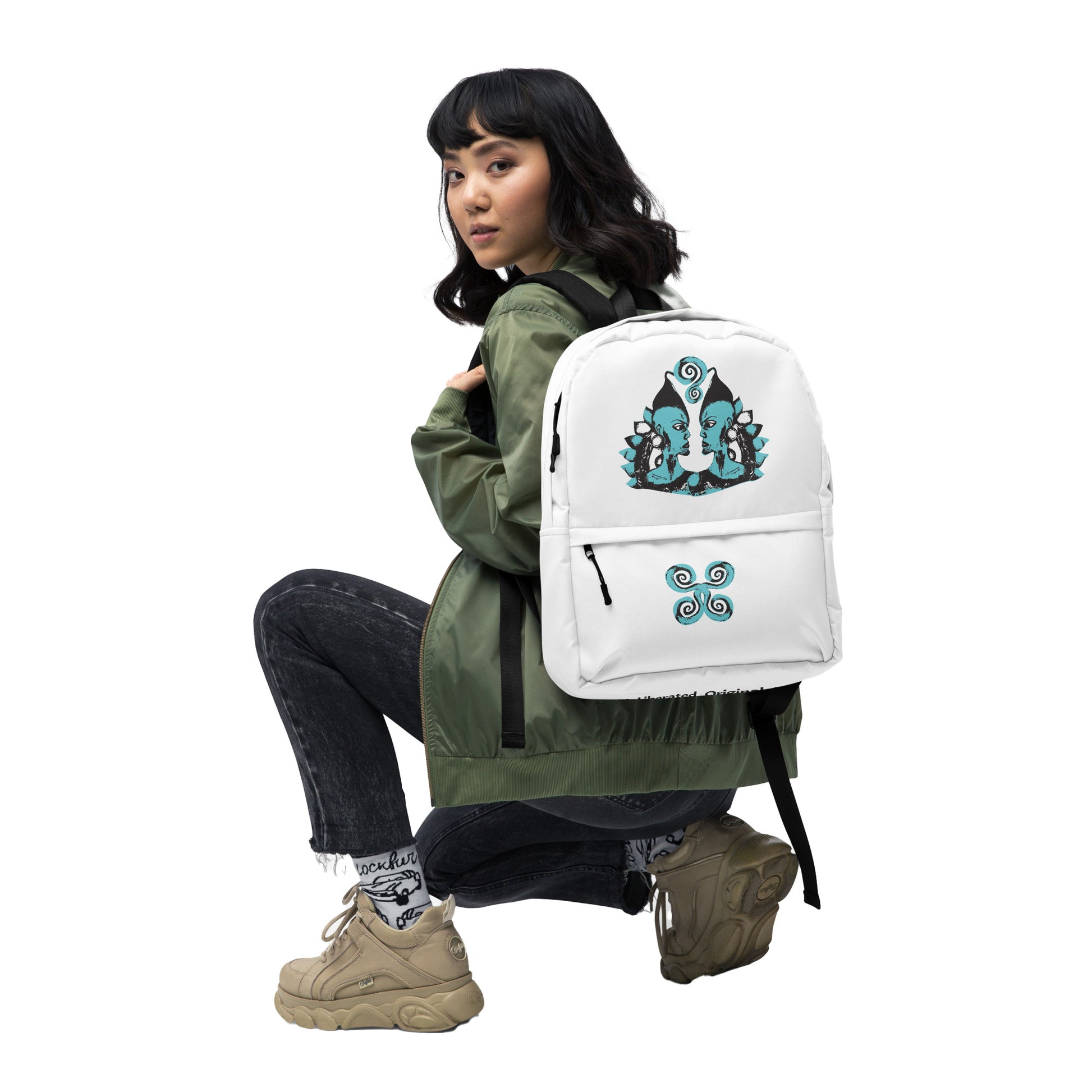 The model wearing a white backpack, featuring a hand-drawn, culturally inspired design of two mirrored faces in bold black and teal on the main panel, and an intricate teal spiral motif on the pocket, celebrating self-expression and individuality in modern bohemian style fashion by K.L.O.E.