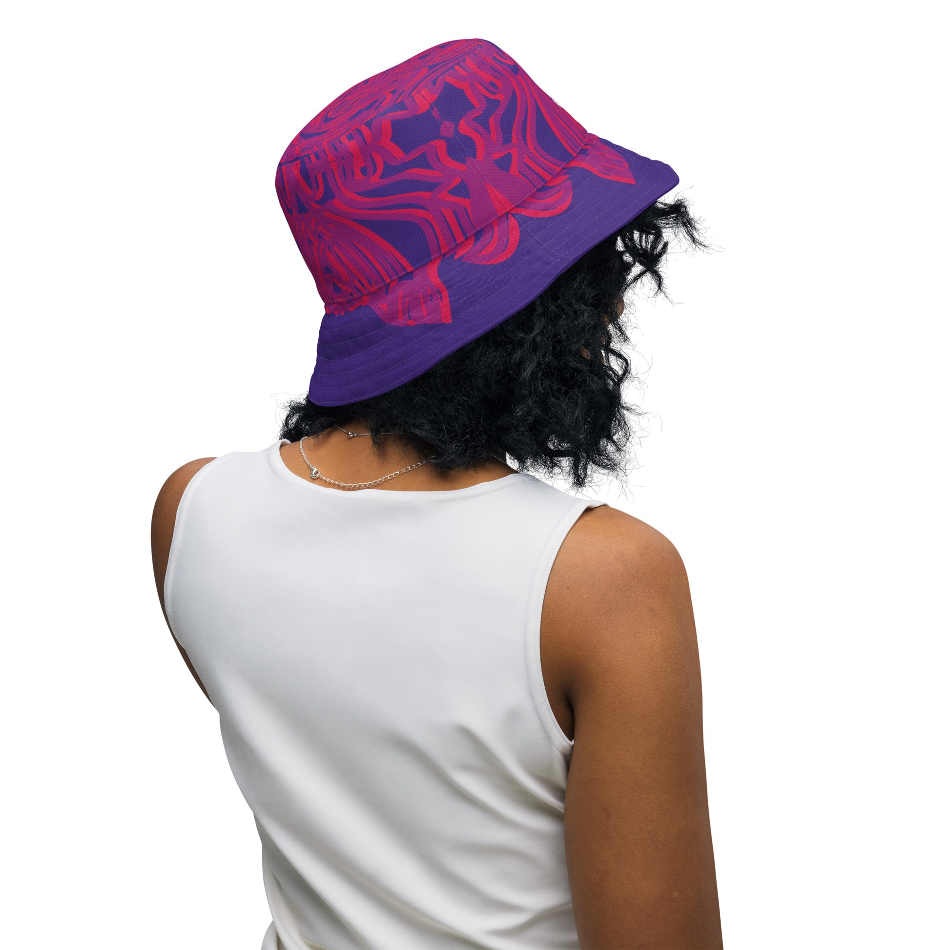 Reversible purple bucket hat with bold orange and red culturally inspired patterns, featuring abstract swirls and mirrored face design — artistic fashion accessory from KLOE’s The Secret Chambers of I & I collection, on a model.