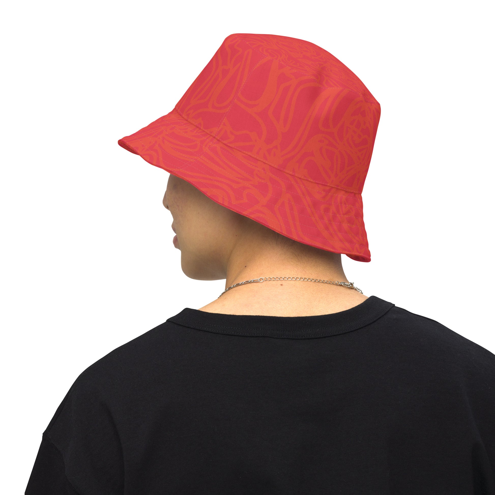 Reversible red-orange bucket hat with cultural swirl design and mirrored face motif on one side, and K.L.O.E wordmark on the other.