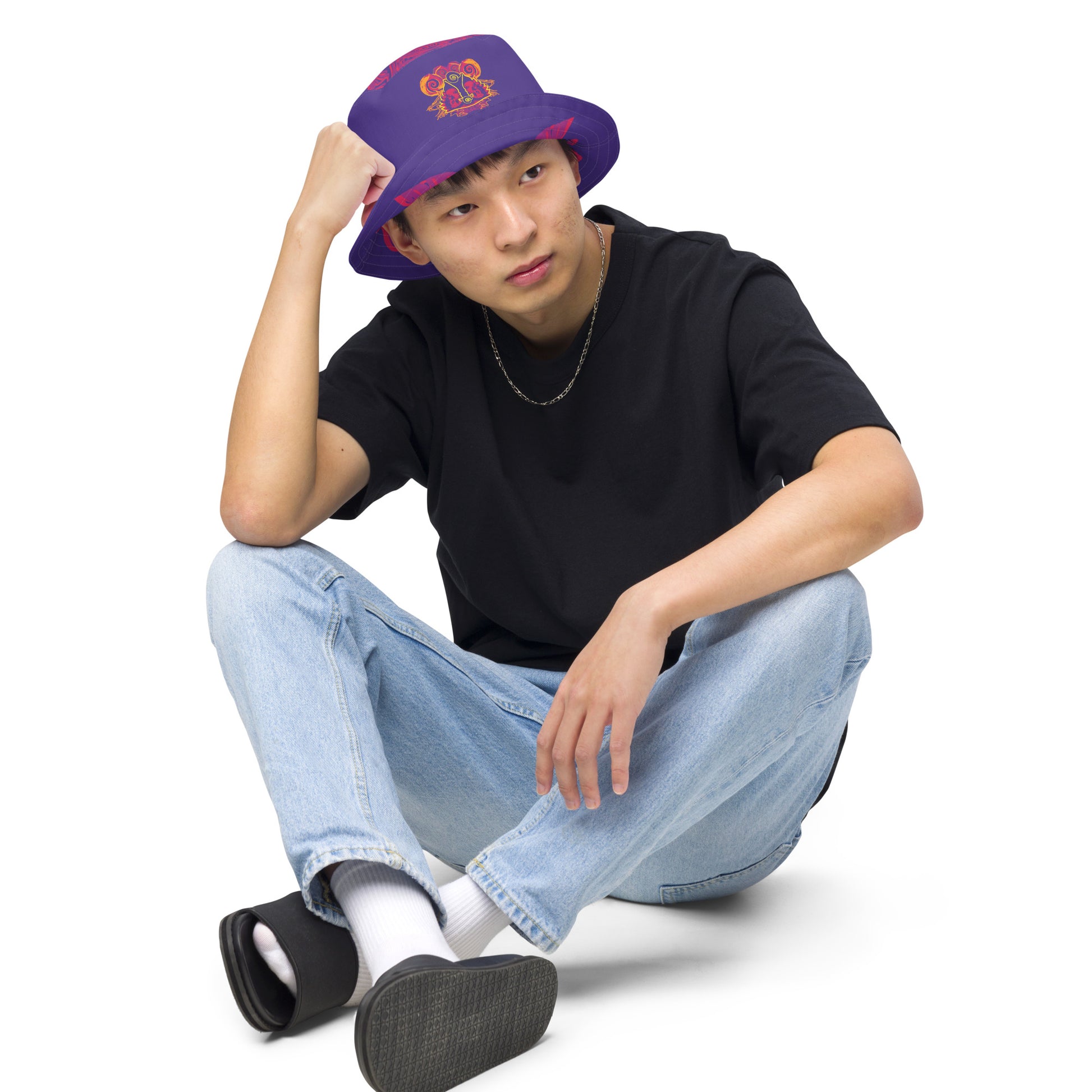 Reversible purple bucket hat with bold orange and red culturally inspired patterns, featuring abstract swirls and mirrored face design — artistic fashion accessory from KLOE’s The Secret Chambers of I & I collection, on a model.