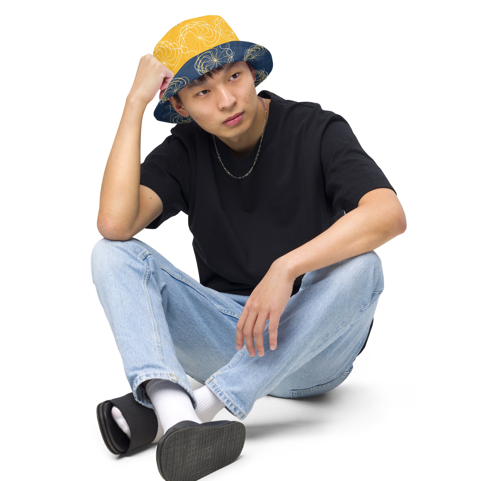 Reversible bucket hat featuring navy and golden yellow sides with abstract white linework and mirrored face emblems, blending hand-drawn cultural art with bold, expressive streetwear style.