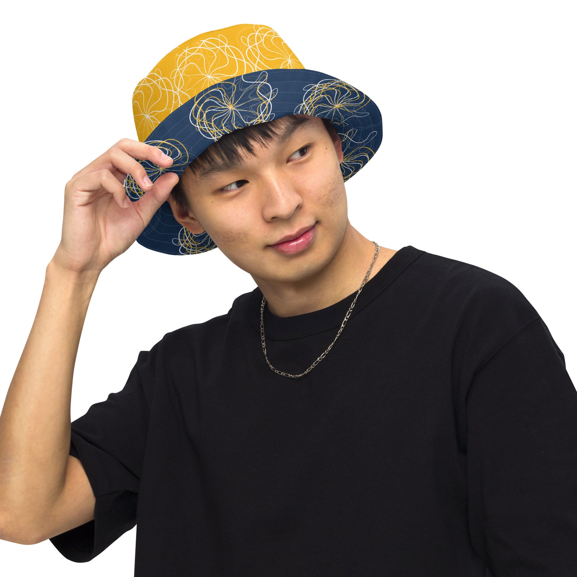 Reversible bucket hat featuring navy and golden yellow sides with abstract white linework and mirrored face emblems, blending hand-drawn cultural art with bold, expressive streetwear style.
