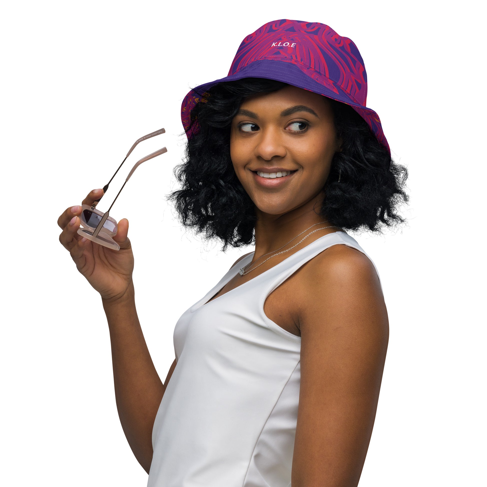 Reversible purple bucket hat with bold orange and red culturally inspired patterns, featuring abstract swirls and mirrored face design — artistic fashion accessory from KLOE’s The Secret Chambers of I & I collection, on a model.