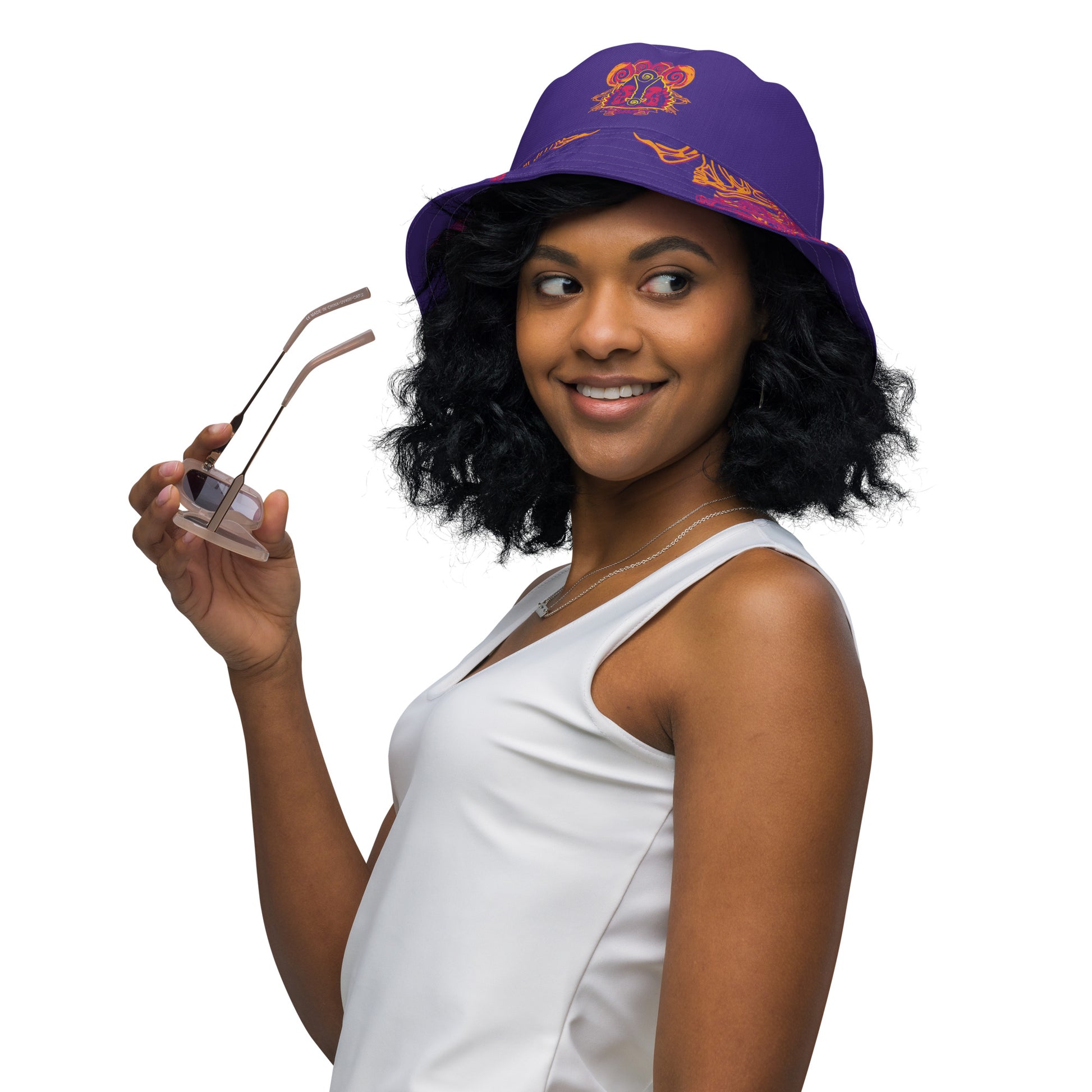 Reversible purple bucket hat with bold orange and red culturally inspired patterns, featuring abstract swirls and mirrored face design — artistic fashion accessory from KLOE’s The Secret Chambers of I & I collection, on a model.
