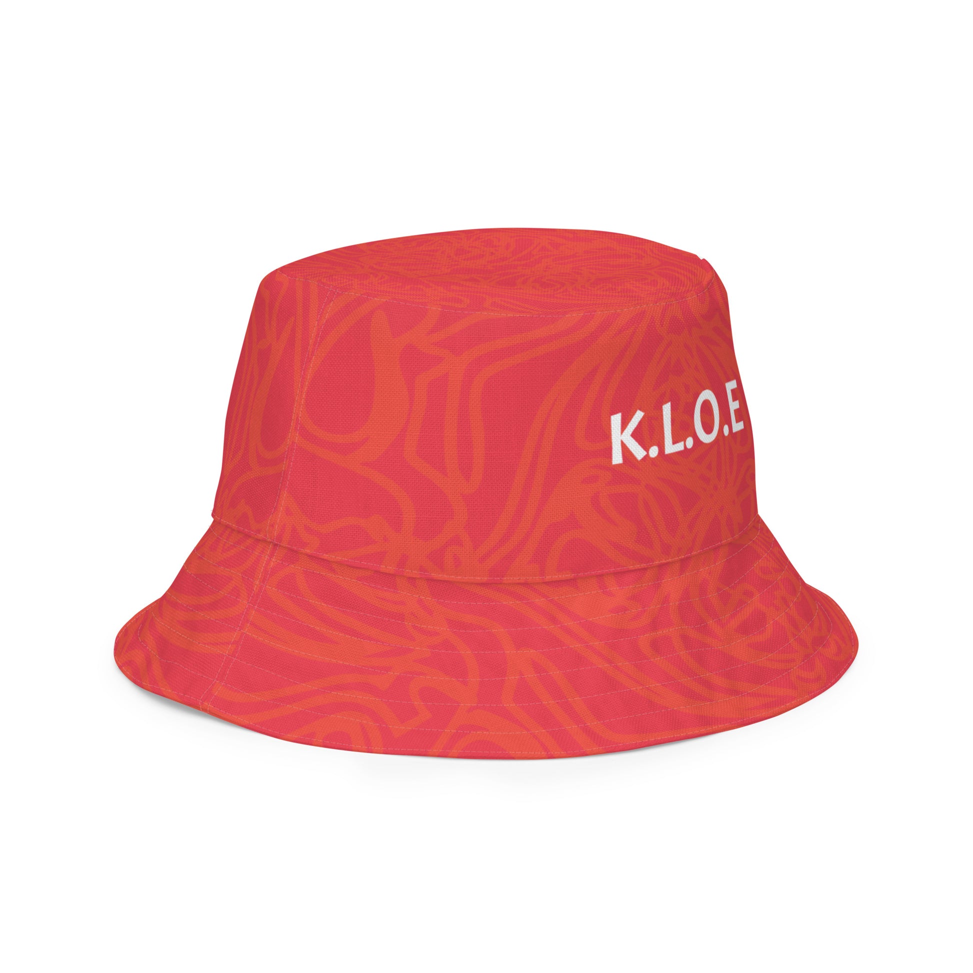 Reversible red-orange bucket hat with cultural swirl design and mirrored face motif on one side, and K.L.O.E wordmark on the other.