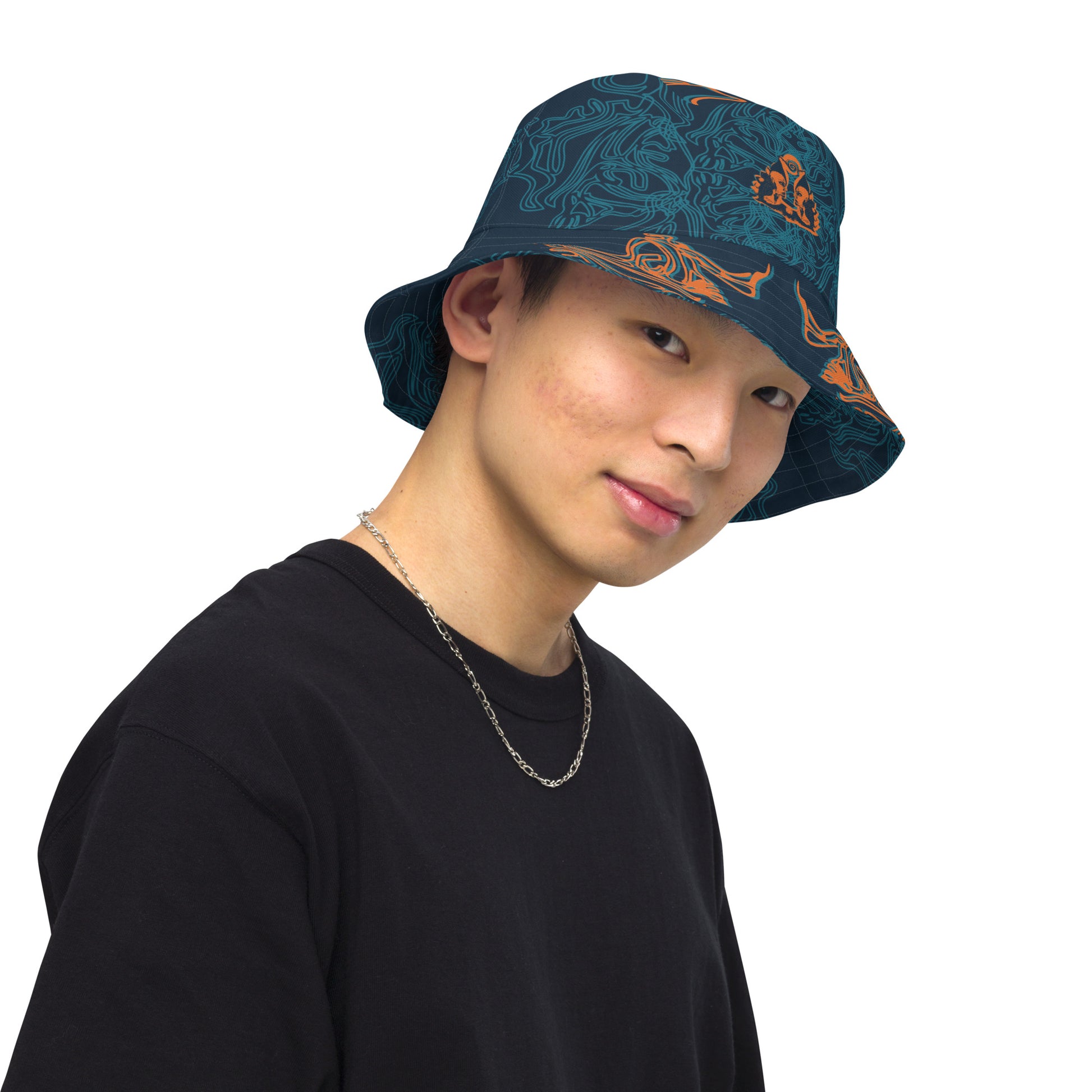 Reversible bucket hat featuring a small orange mirrored face motif and bold tribal-inspired patterns, blending art and streetwear.