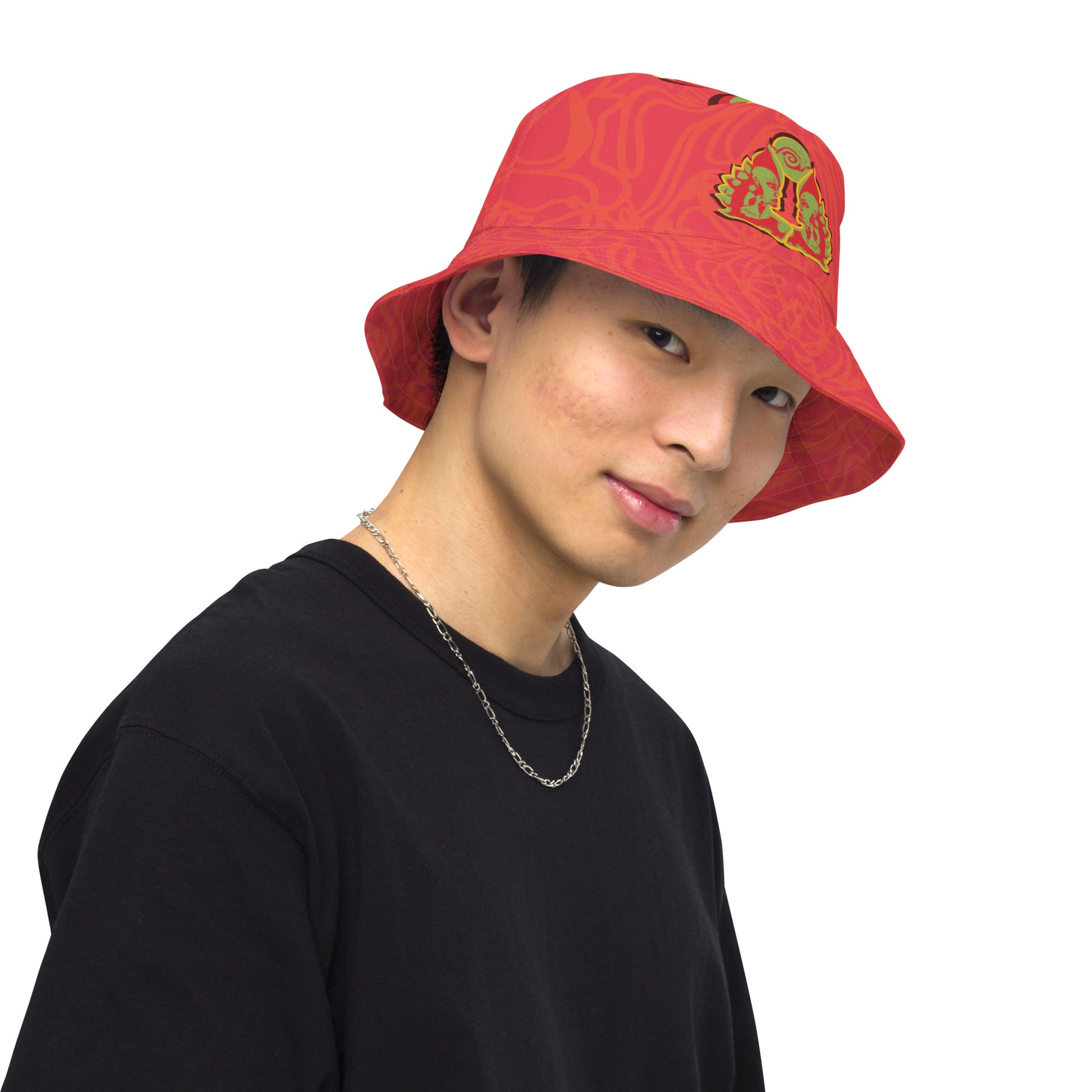 Reversible red-orange bucket hat with cultural swirl design and mirrored face motif on one side, and K.L.O.E wordmark on the other.