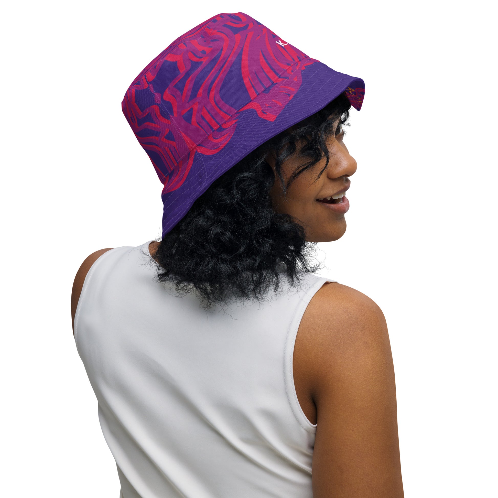 Reversible purple bucket hat with bold orange and red culturally inspired patterns, featuring abstract swirls and mirrored face design — artistic fashion accessory from KLOE’s The Secret Chambers of I & I collection, on a model.