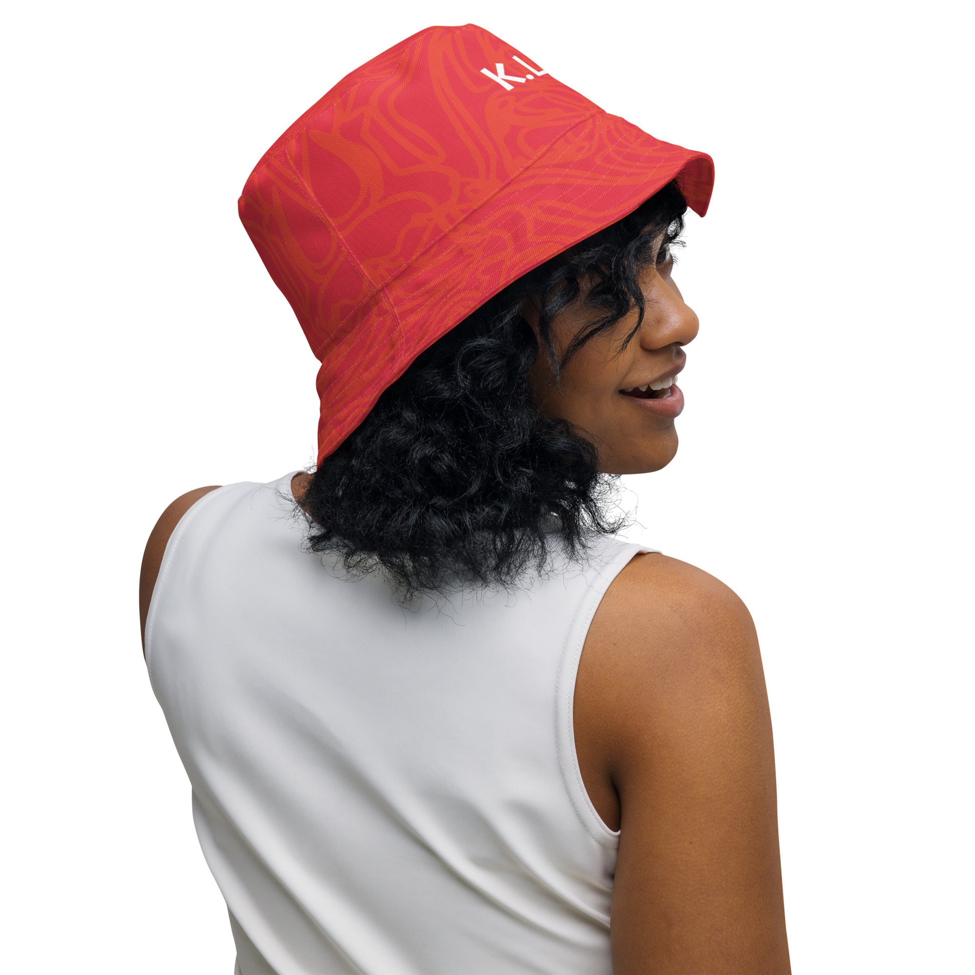 Reversible red-orange bucket hat with cultural swirl design and mirrored face motif on one side, and K.L.O.E wordmark on the other.