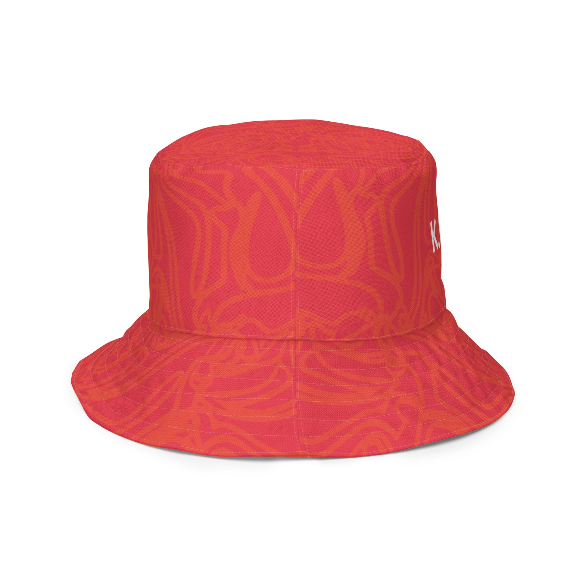 Reversible red-orange bucket hat with cultural swirl design and mirrored face motif on one side, and K.L.O.E wordmark on the other.