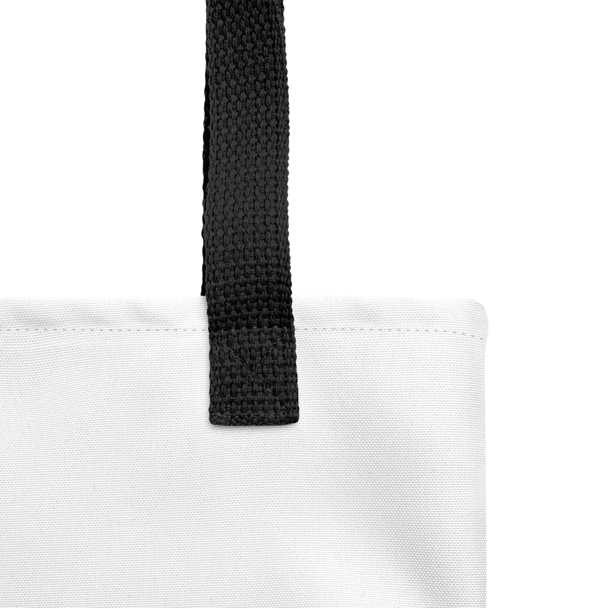 Detail view of a white tote bag with a bold K.L.O.E. hand-drawn design featuring two mirrored faces in black and teal, highlighting cultural inspiration, individuality, and modern bohemian self-expression.