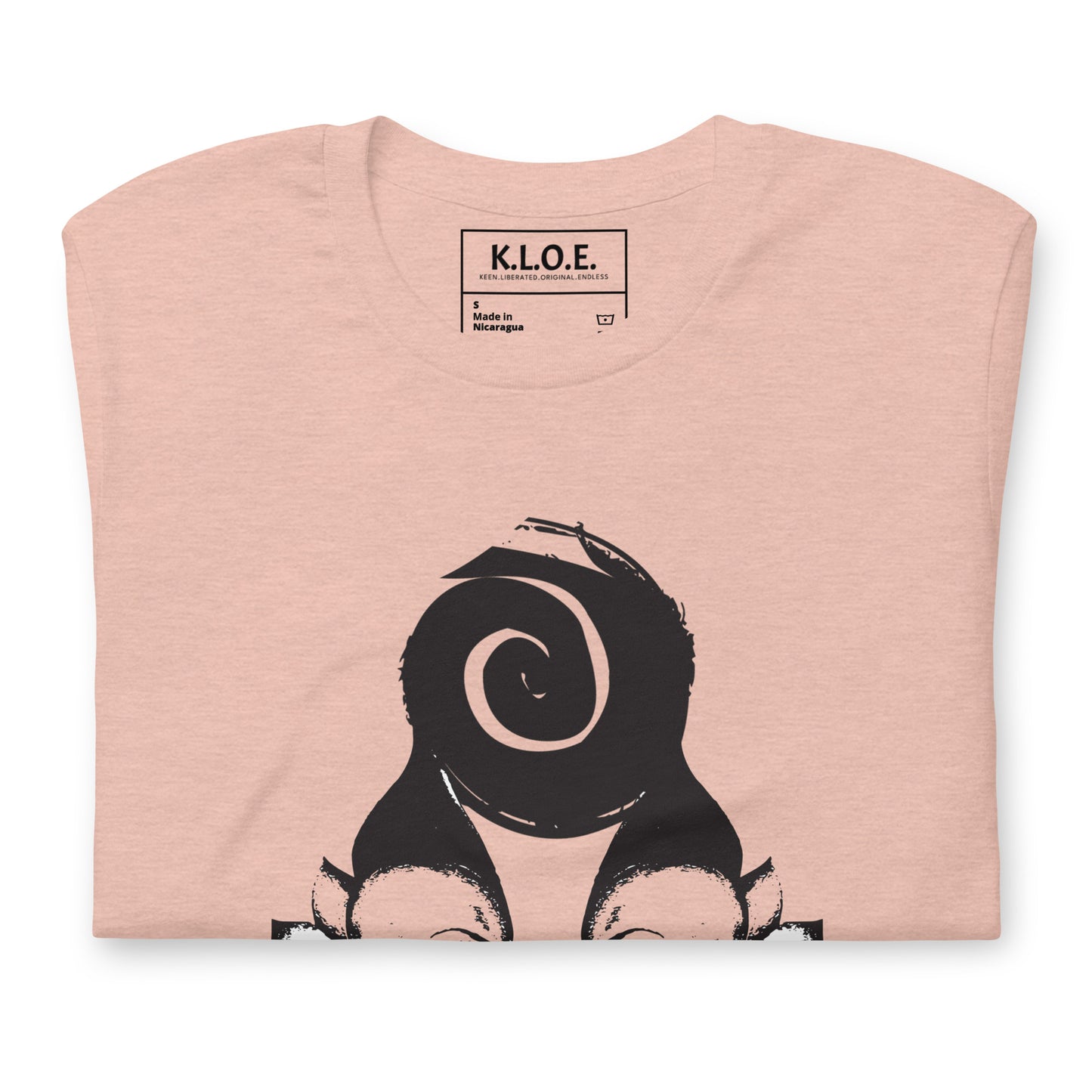 Folded peach color t-shirt featuring a hand-drawn black ink design of two mirrored female figures with bold, intricate headpieces, connected by a swirling central element. This artistic piece from K.L.O.E. embraces cultural inspiration and self-expression, crafted for those who appreciate unique, expressive fashion and modern bohemian style.