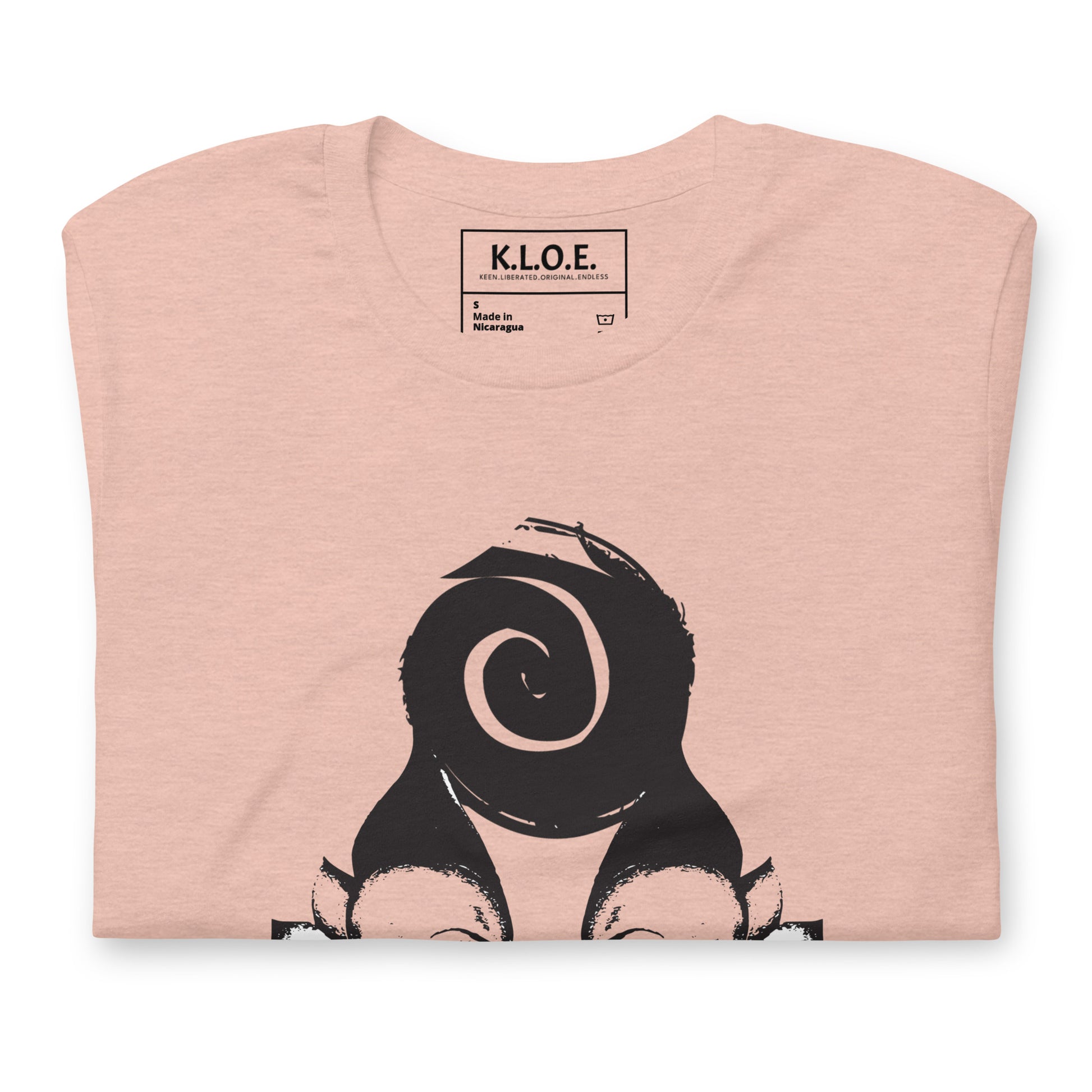 Folded peach color t-shirt featuring a hand-drawn black ink design of two mirrored female figures with bold, intricate headpieces, connected by a swirling central element. This artistic piece from K.L.O.E. embraces cultural inspiration and self-expression, crafted for those who appreciate unique, expressive fashion and modern bohemian style.