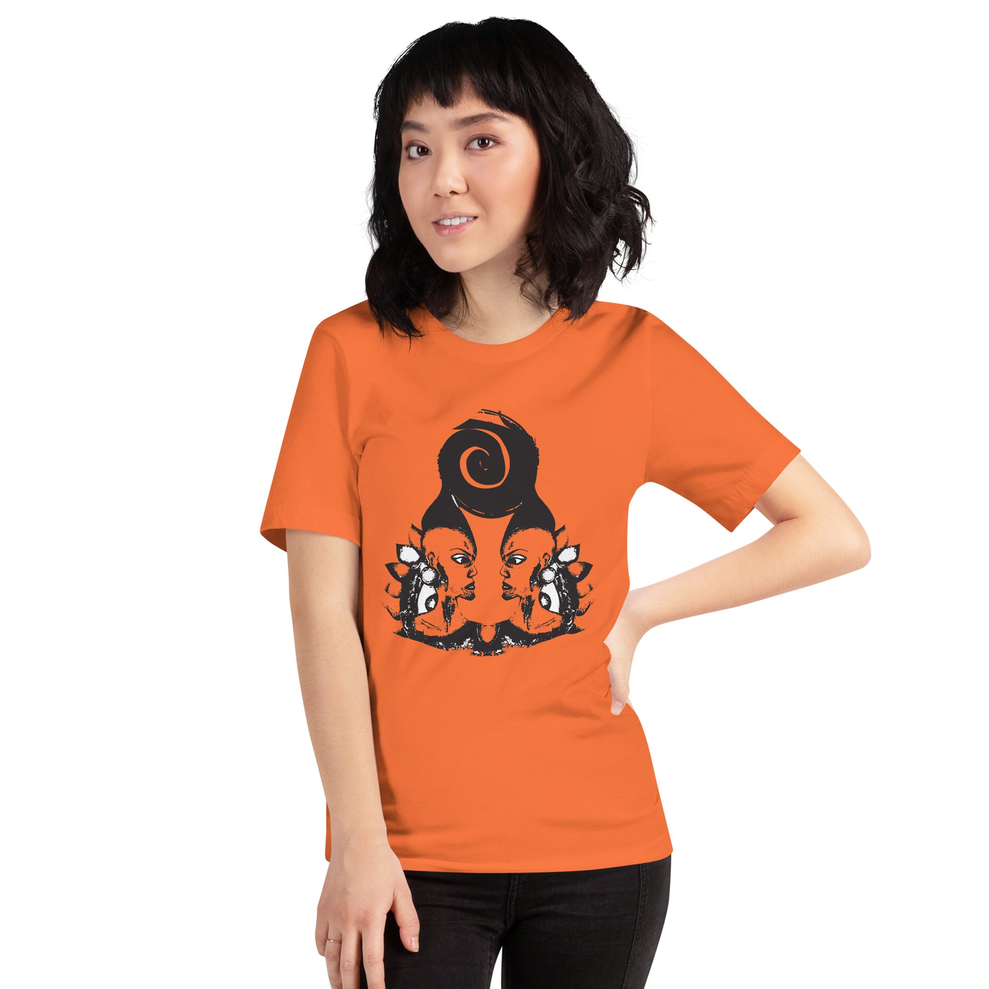 A model wearing orange t-shirt featuring a hand-drawn black ink design of two mirrored female figures with bold, intricate headpieces, connected by a swirling central element. This artistic piece from K.L.O.E. embraces cultural inspiration and self-expression, crafted for those who appreciate unique, expressive fashion and modern bohemian style.