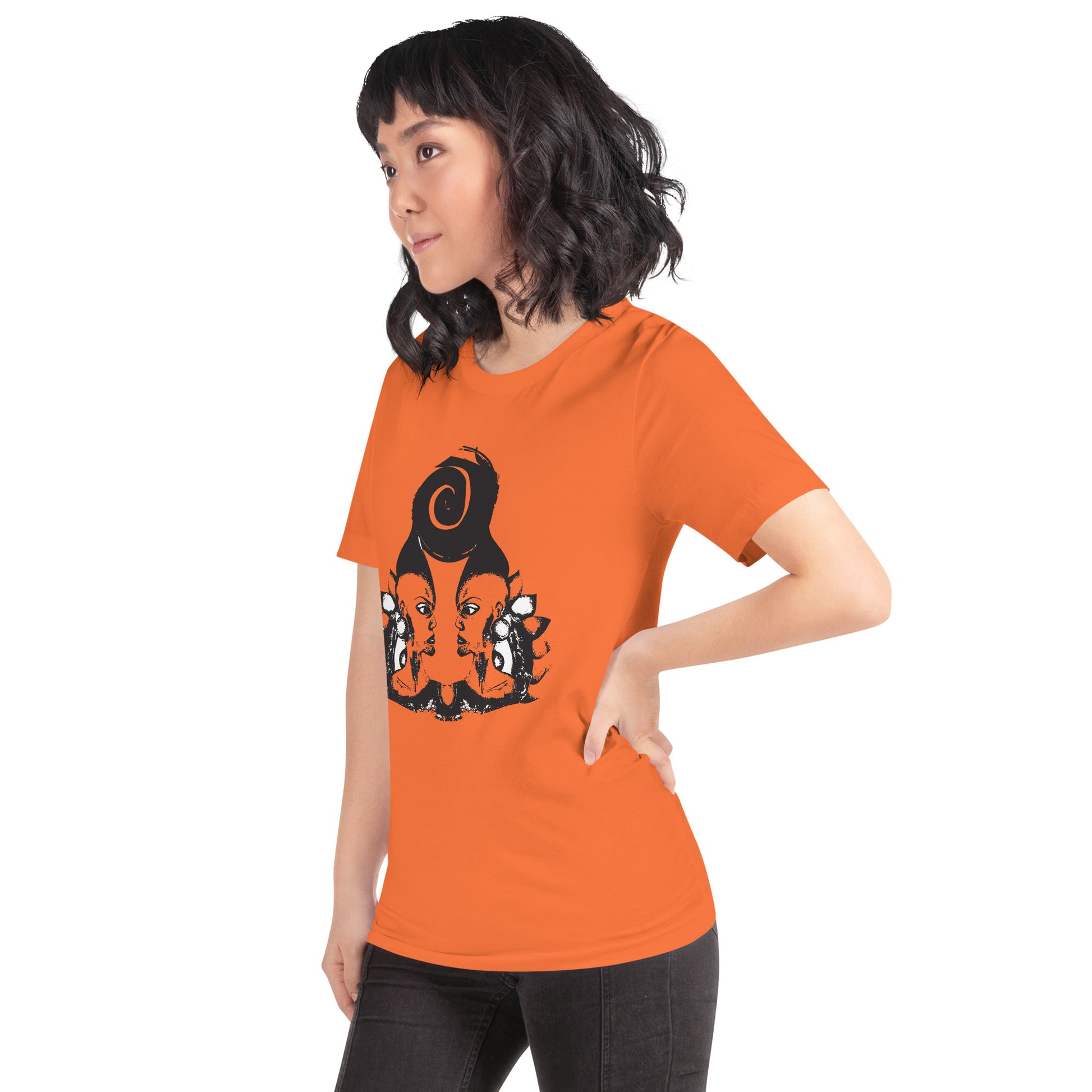 A model wearing orange t-shirt featuring a hand-drawn black ink design of two mirrored female figures with bold, intricate headpieces, connected by a swirling central element. This artistic piece from K.L.O.E. embraces cultural inspiration and self-expression, crafted for those who appreciate unique, expressive fashion and modern bohemian style.