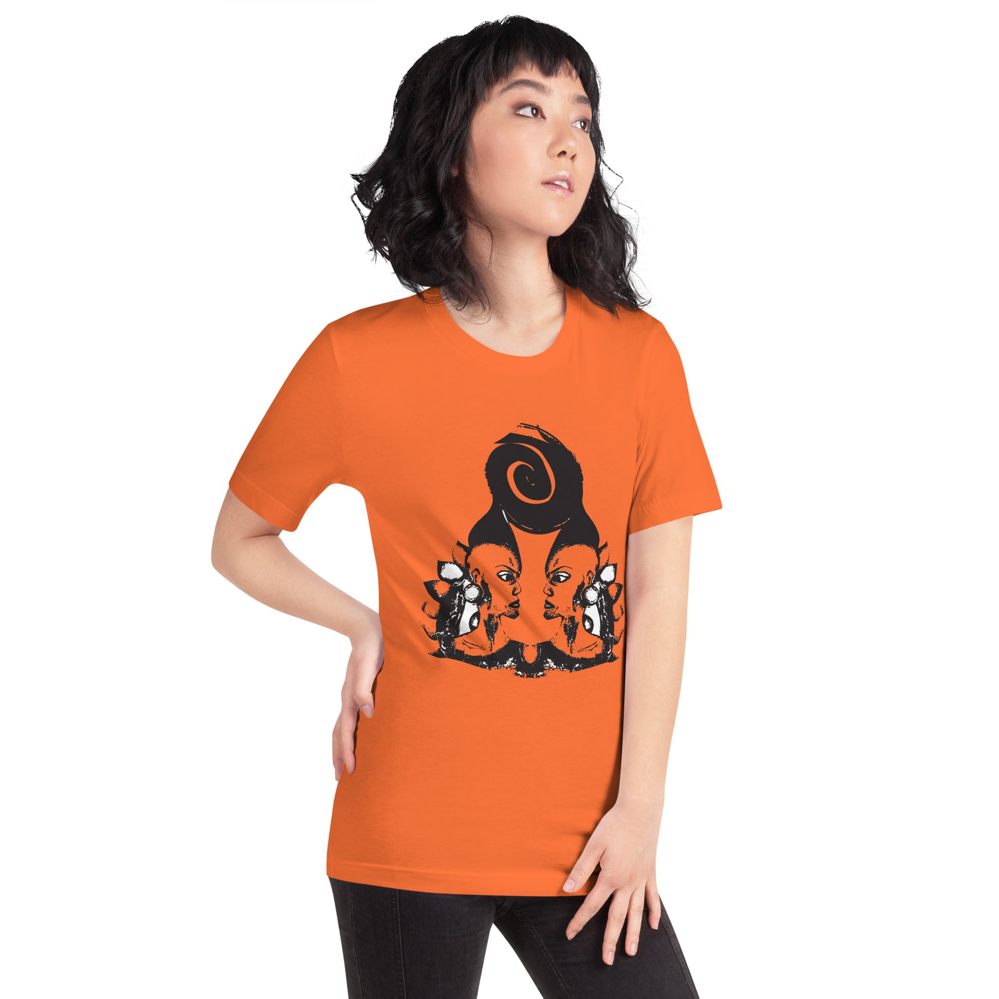 A model wearing orange t-shirt featuring a hand-drawn black ink design of two mirrored female figures with bold, intricate headpieces, connected by a swirling central element. This artistic piece from K.L.O.E. embraces cultural inspiration and self-expression, crafted for those who appreciate unique, expressive fashion and modern bohemian style.