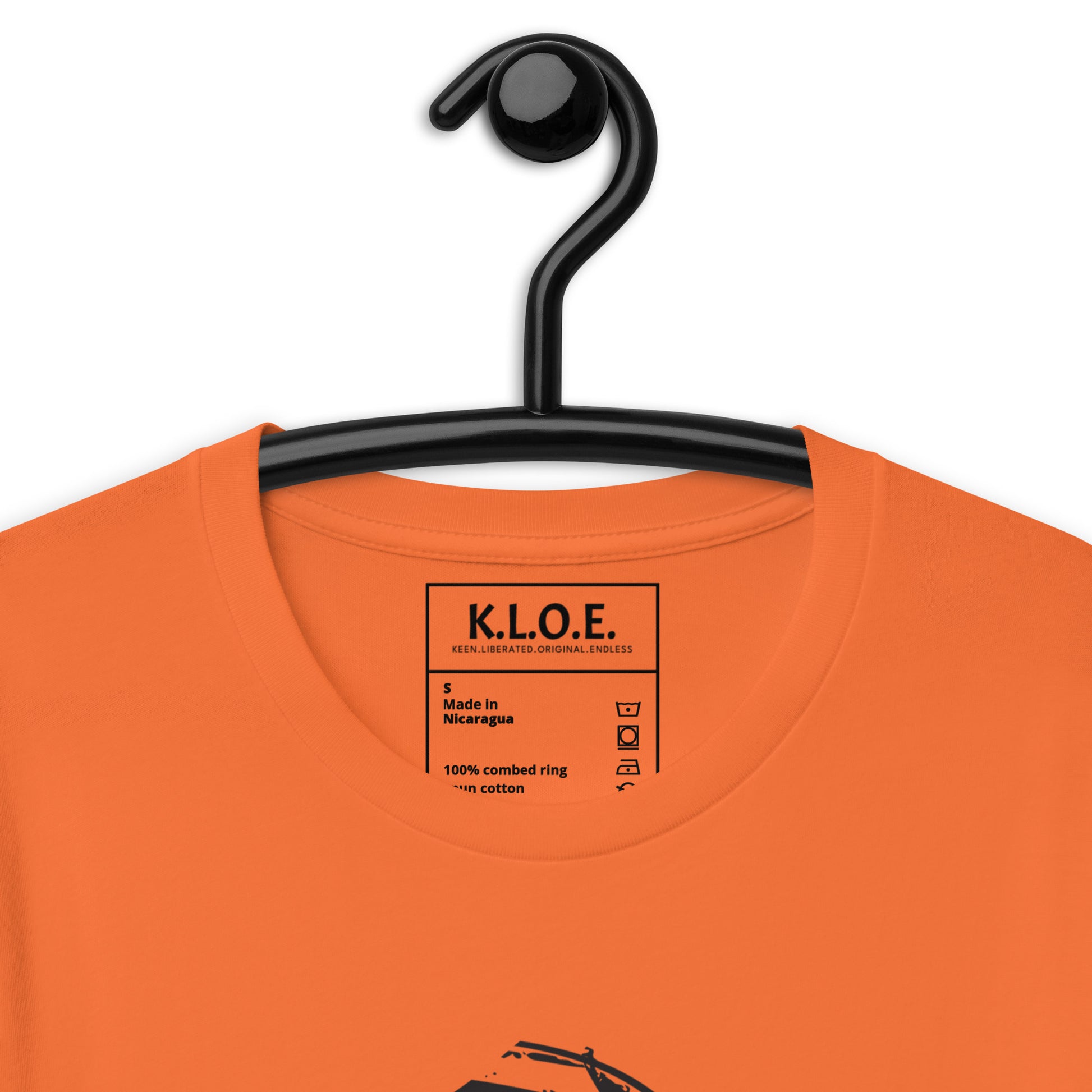 Orange t-shirt, on a hanger, featuring a hand-drawn black ink design of two mirrored female figures with bold, intricate headpieces, connected by a swirling central element. This artistic piece from K.L.O.E. embraces cultural inspiration and self-expression, crafted for those who appreciate unique, expressive fashion and modern bohemian style. Detail view, showing the inside label.