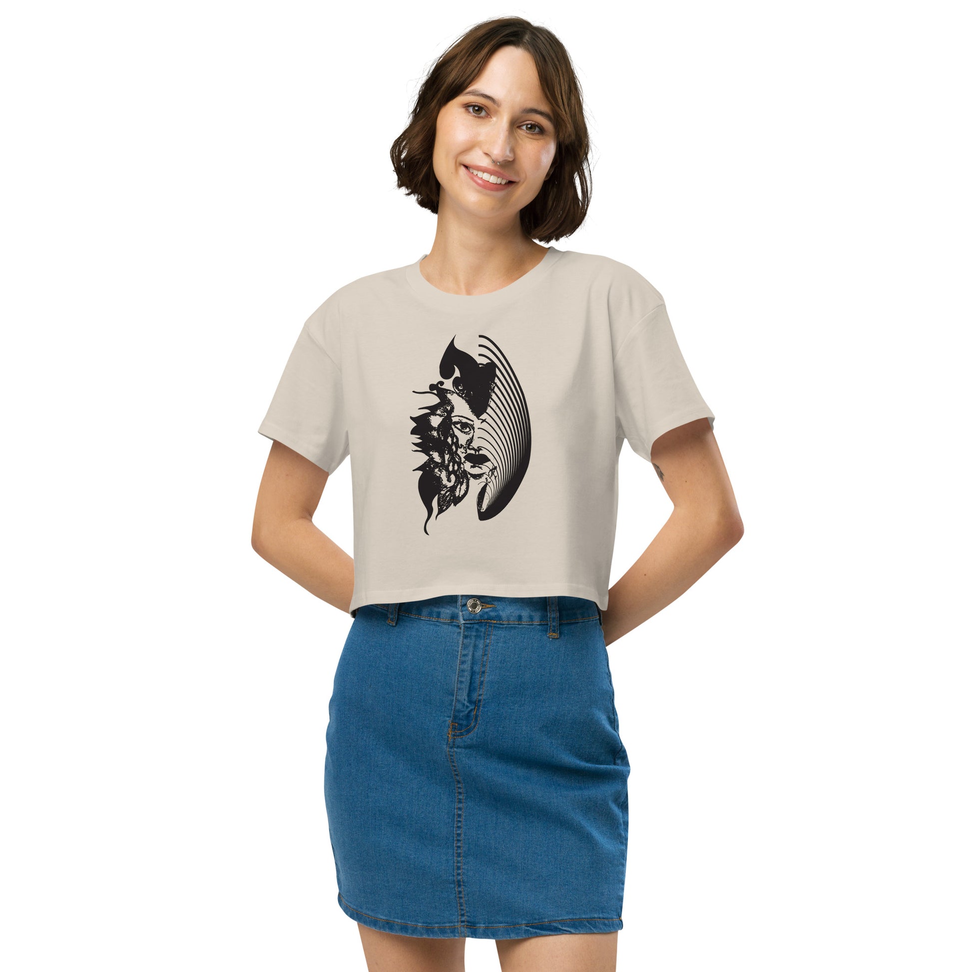 A model wearing a bone K.L.O.E. crop t-shirt featuring a culturally inspired, hand-drawn black graphic of a bold, expressive face surrounded by intricate details, celebrating individuality and artistic self-expression in modern bohemian style fashion.