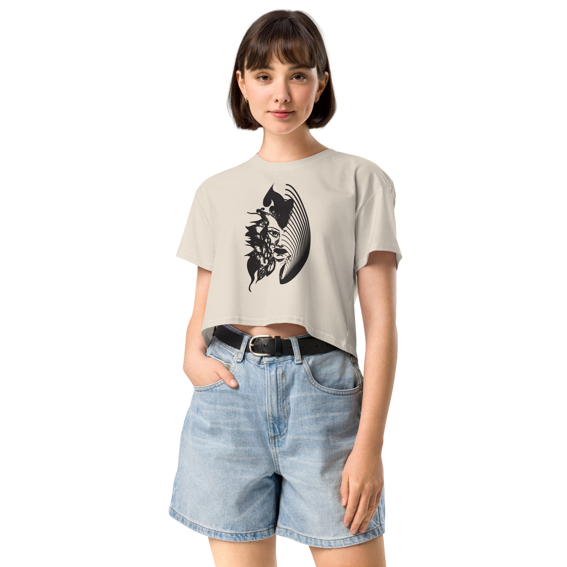 A model wearing a bone K.L.O.E. crop t-shirt featuring a culturally inspired, hand-drawn black graphic of a bold, expressive face surrounded by intricate details, celebrating individuality and artistic self-expression in modern bohemian style fashion.