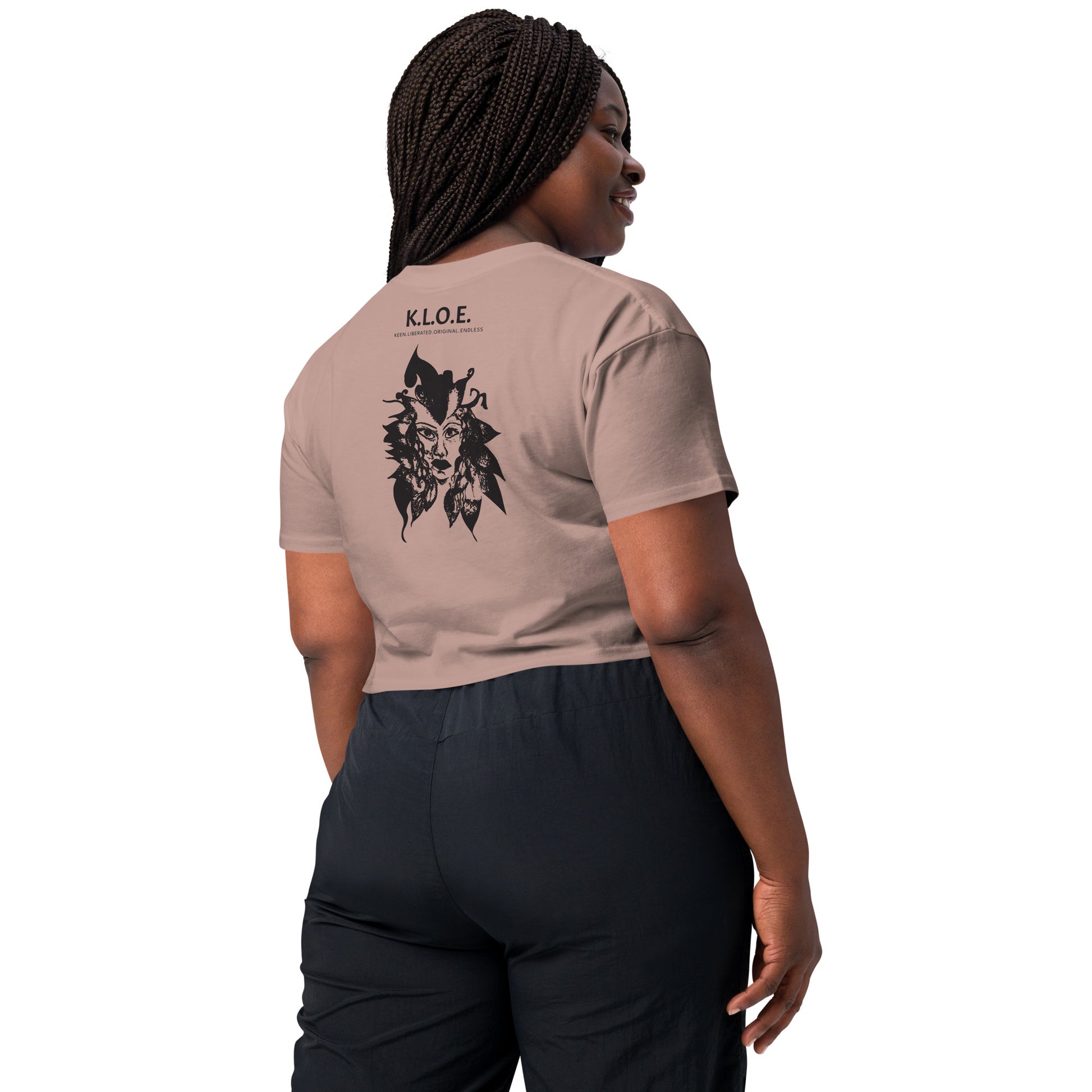 Back view of a hazy pink K.L.O.E. crop t-shirt showcasing a culturally inspired, hand-drawn black design featuring a bold, expressive face intertwined with flowing, abstract patterns, and K.L.O.E. logo, embodying artistic self-expression and modern bohemian style fashion, on a model.