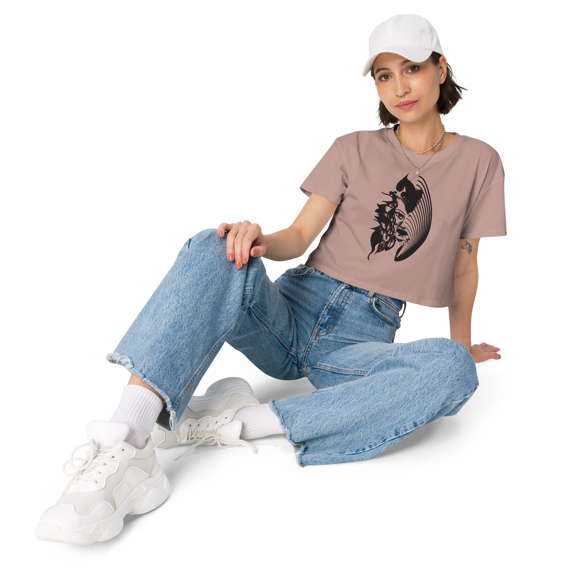 A model wearing hazy pink K.L.O.E. crop t-shirt featuring a culturally inspired, hand-drawn black graphic of a bold, expressive face surrounded by intricate details, celebrating individuality and artistic self-expression in modern bohemian style fashion.