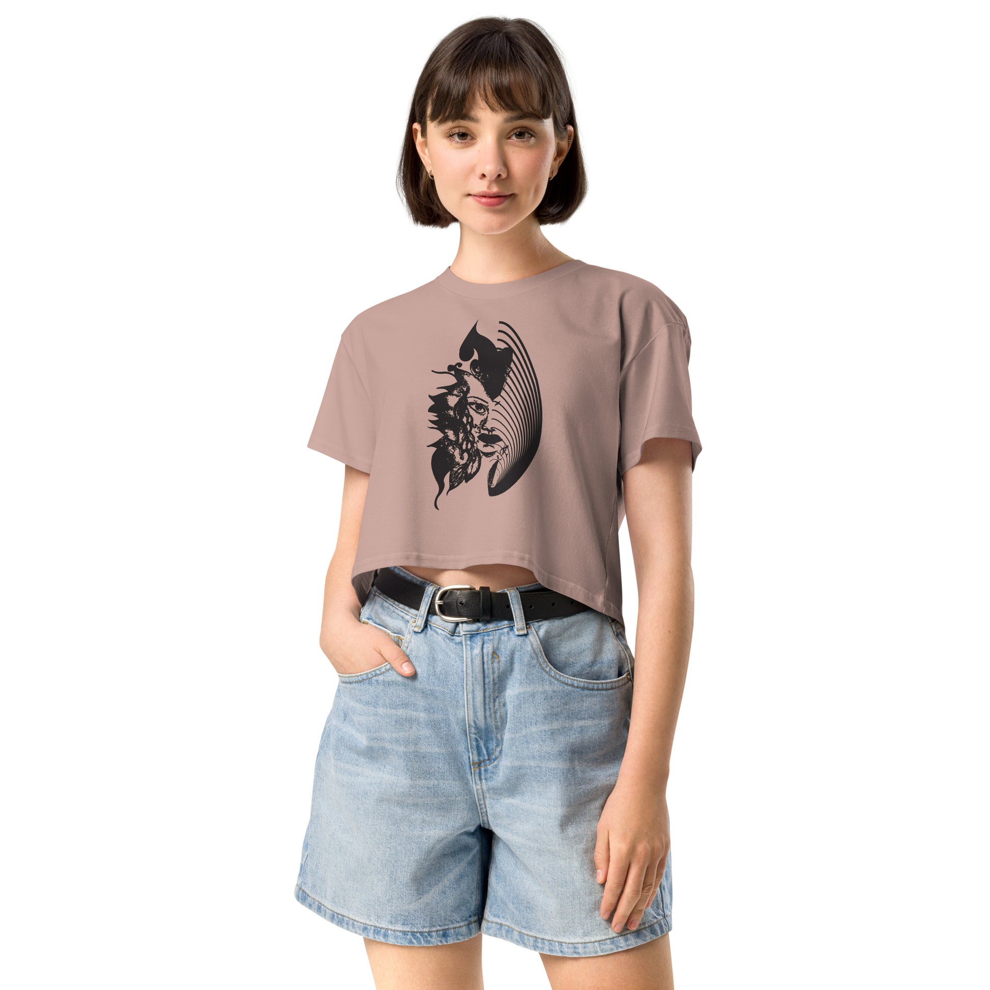 A model wearing hazy pink K.L.O.E. crop t-shirt featuring a culturally inspired, hand-drawn black graphic of a bold, expressive face surrounded by intricate details, celebrating individuality and artistic self-expression in modern bohemian style fashion.