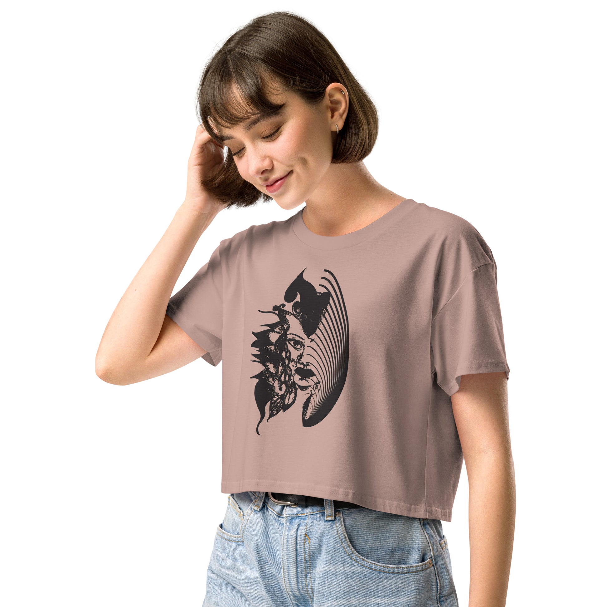 A model wearing hazy pink K.L.O.E. crop t-shirt featuring a culturally inspired, hand-drawn black graphic of a bold, expressive face surrounded by intricate details, celebrating individuality and artistic self-expression in modern bohemian style fashion.