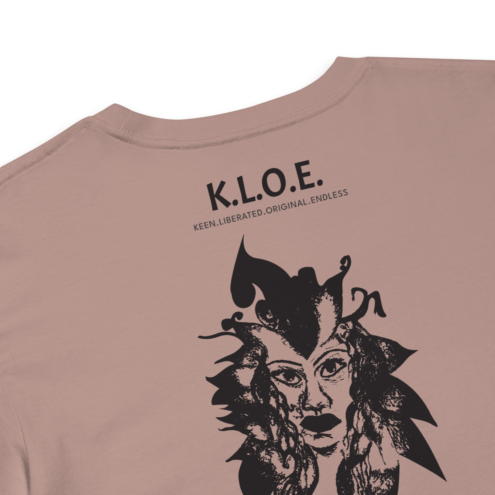 Detail view of a back side of a hazy pink K.L.O.E. crop t-shirt showcasing a culturally inspired, hand-drawn black design featuring a bold, expressive face intertwined with flowing, abstract patterns, and K.L.O.E. logo, embodying artistic self-expression and modern bohemian style fashion.