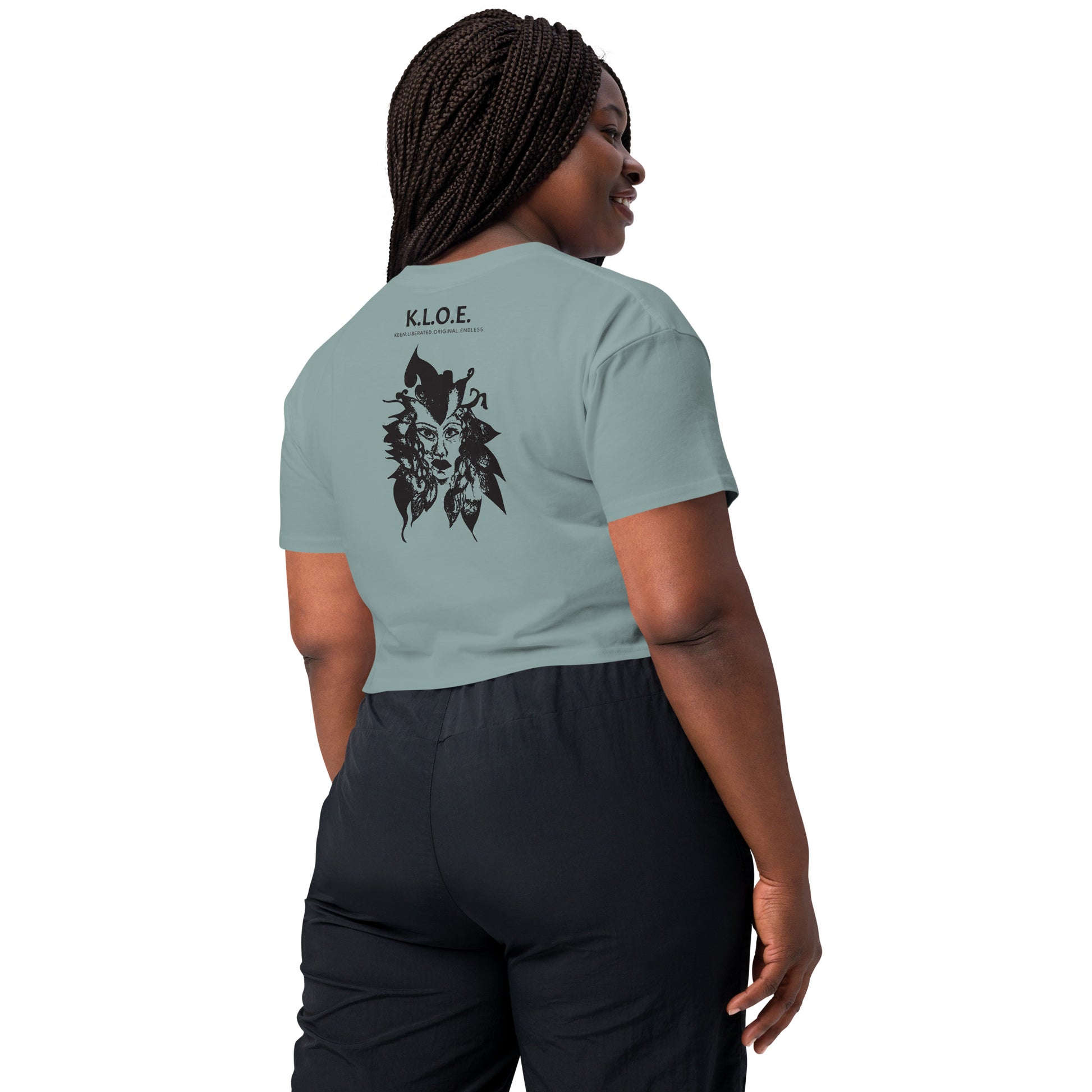 Back view of a mineral K.L.O.E. crop t-shirt showcasing a culturally inspired, hand-drawn black design featuring a bold, expressive face intertwined with flowing, abstract patterns, and K.L.O.E. logo, embodying artistic self-expression and modern bohemian style fashion, on a model.