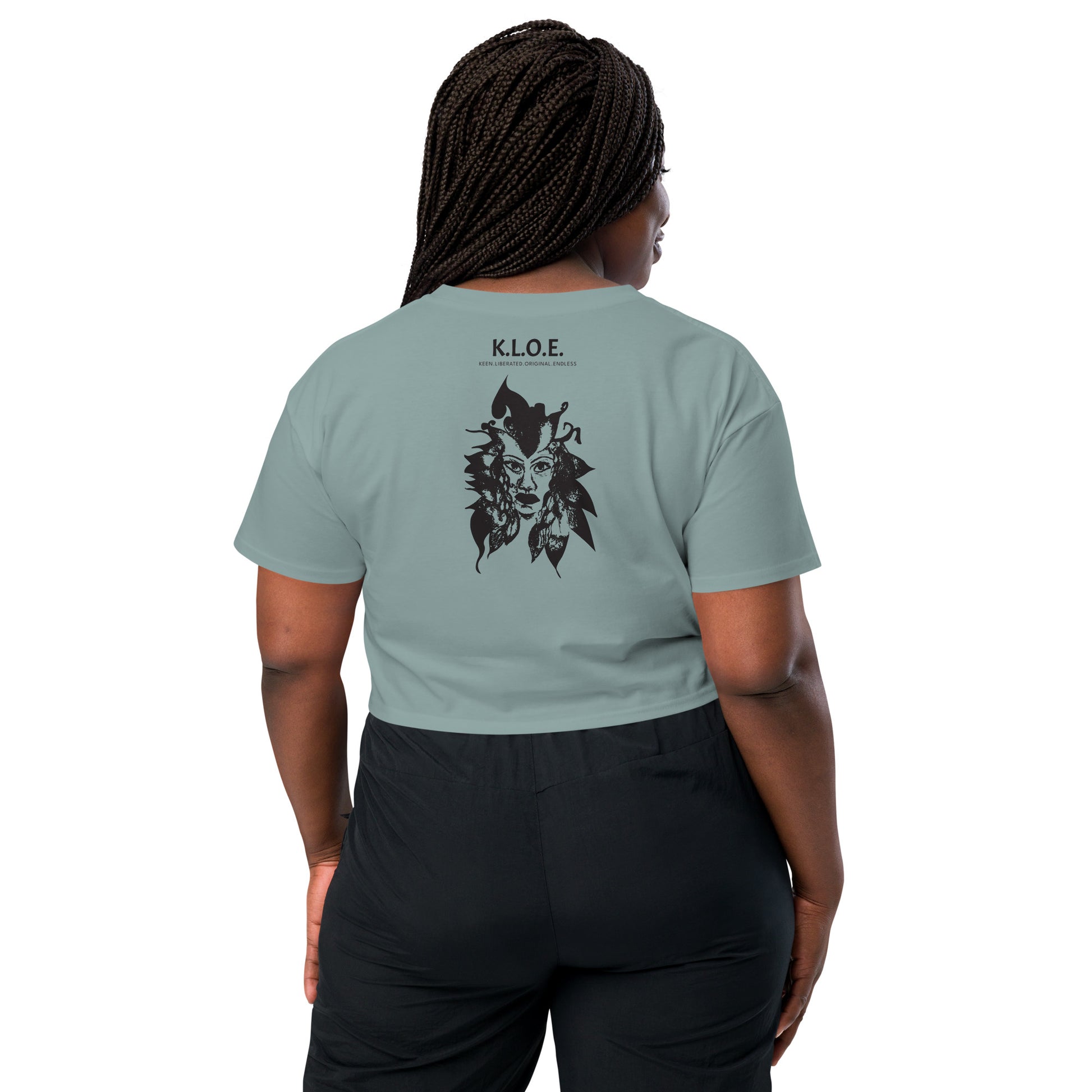 Back view of a mineral K.L.O.E. crop t-shirt showcasing a culturally inspired, hand-drawn black design featuring a bold, expressive face intertwined with flowing, abstract patterns, and K.L.O.E. logo, embodying artistic self-expression and modern bohemian style fashion, on a model.
