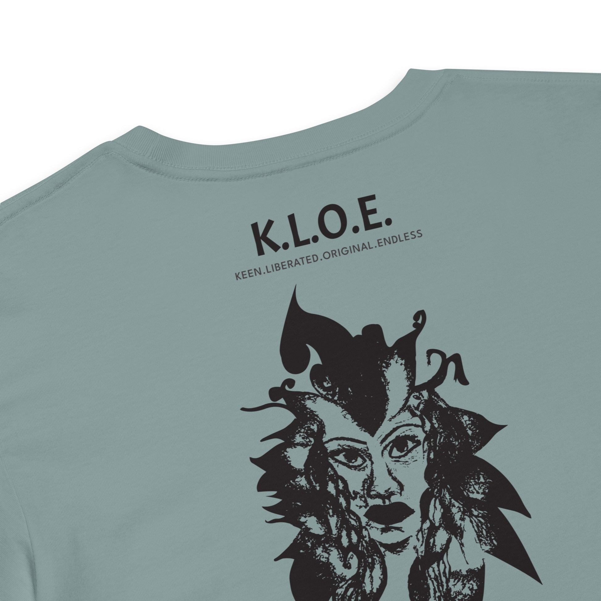Detail view of a back side of a mineral K.L.O.E. crop t-shirt showcasing a culturally inspired, hand-drawn black design featuring a bold, expressive face intertwined with flowing, abstract patterns, and K.L.O.E. logo, embodying artistic self-expression and modern bohemian style fashion.