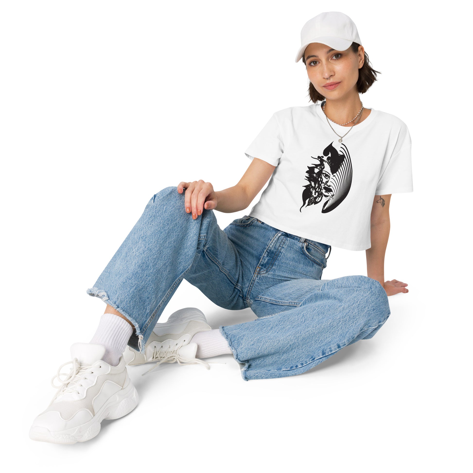 A model wearing white K.L.O.E. crop t-shirt featuring a culturally inspired, hand-drawn black graphic of a bold, expressive face surrounded by intricate details, celebrating individuality and artistic self-expression in modern bohemian style fashion.